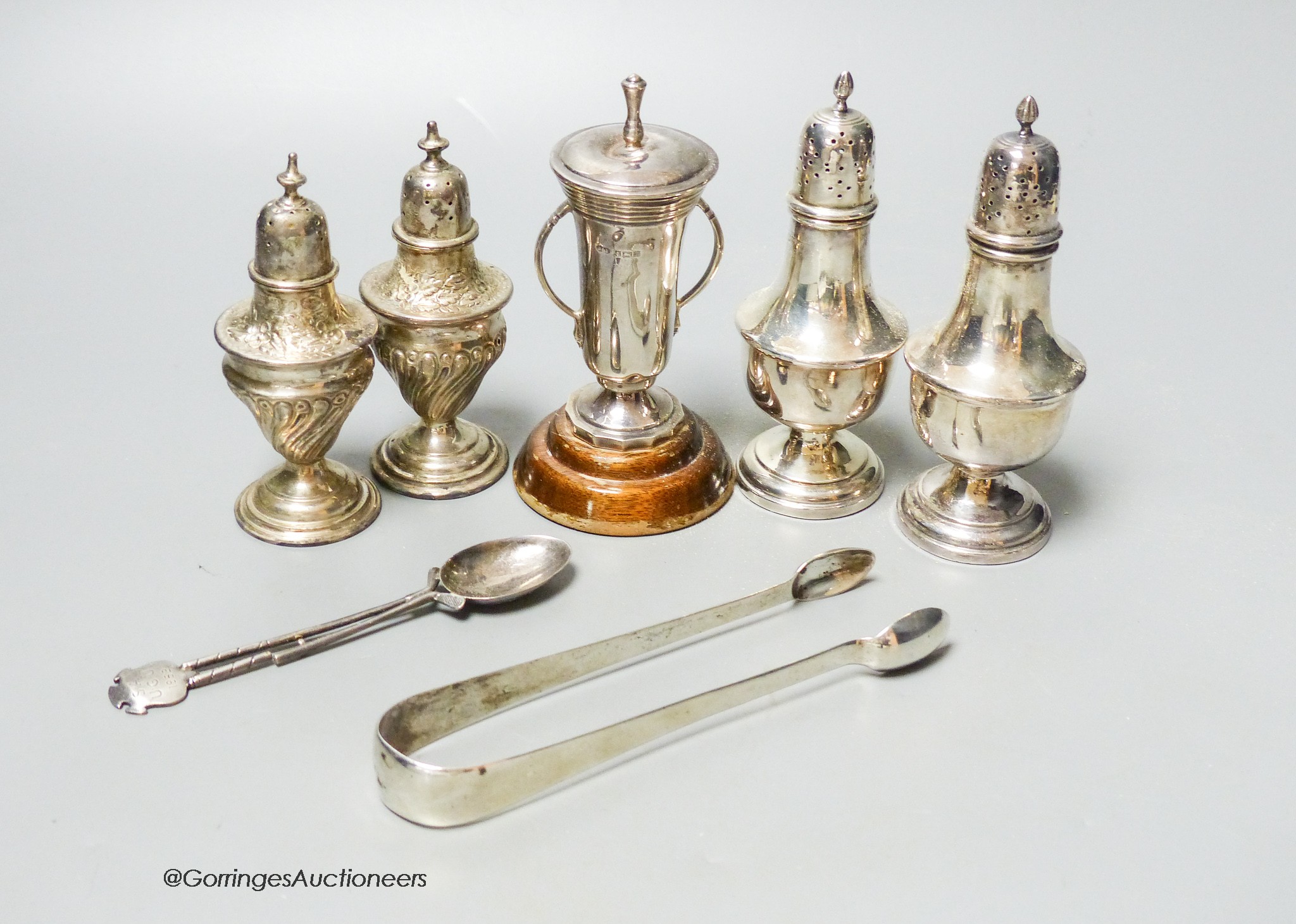 Two pairs of silver peppers, a small silver golfing trophy cup and a pair of silver sugar tongs and a teaspoon, weighable silver 6oz.